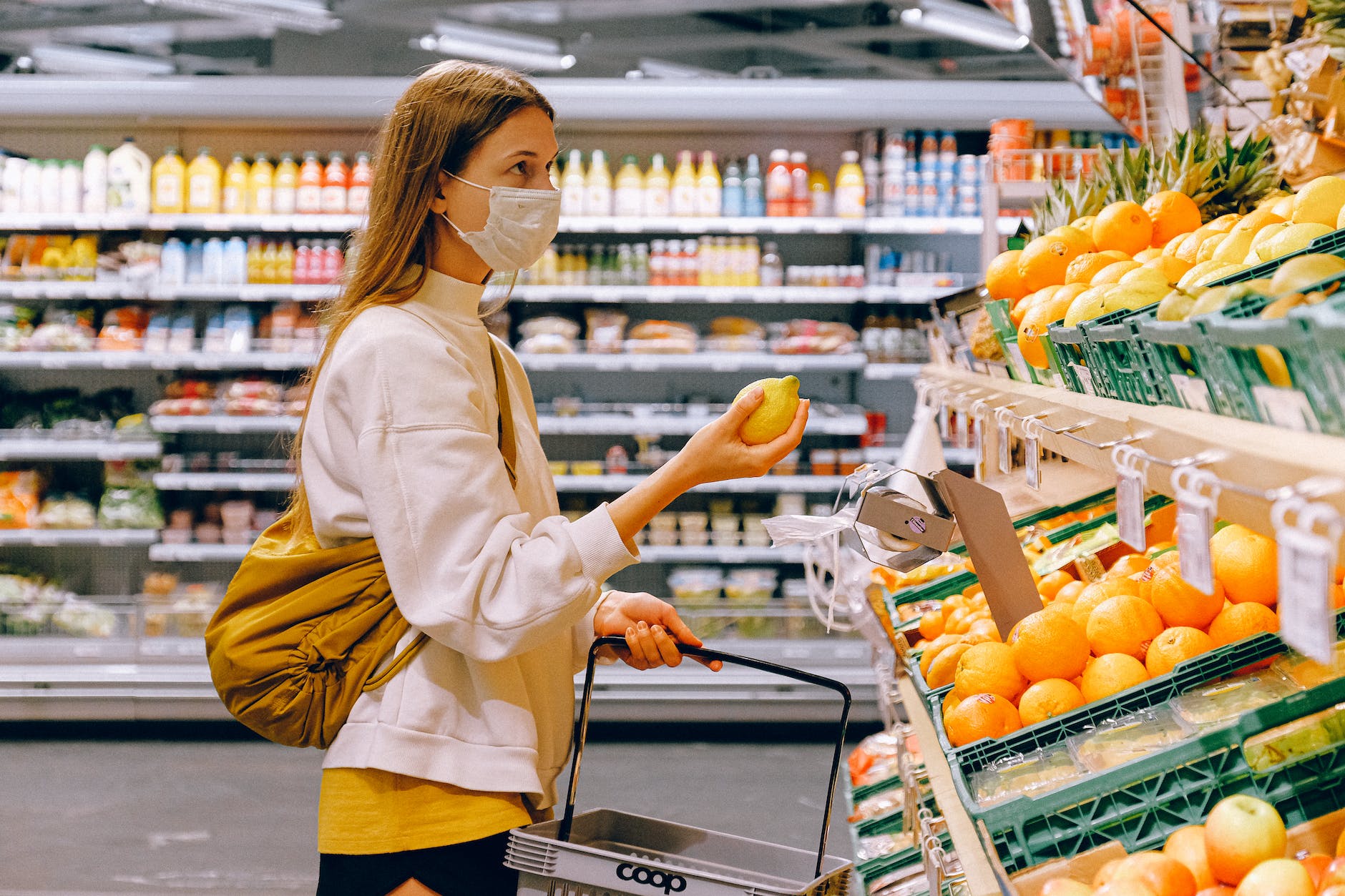 woman in yellow tshirt and beige jacket holding a fruit stand